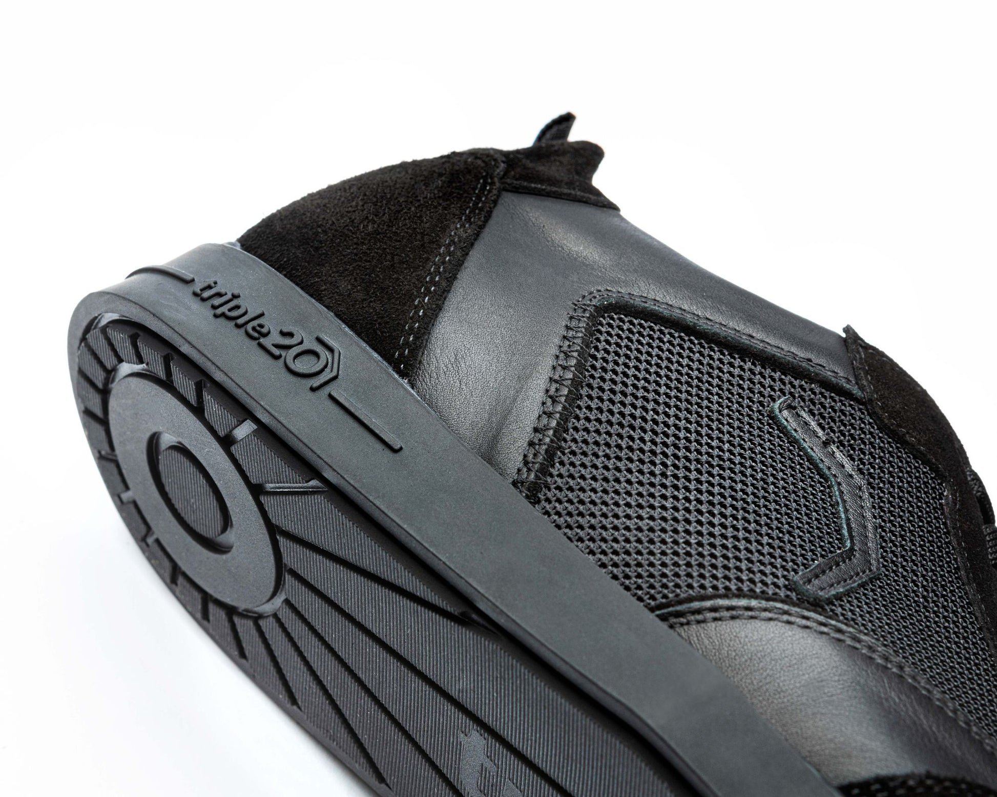 Nahaufnahme eines speziellen Dartschuhs von triple20, der komplett in schwarz gehalten ist. Der Schuh liegt auf der Seite, gut zu sehen ist der Markenschriftzug, der sich in 3D-Optik seitlich auf der Sohle befindet. Ferner lässt sich das aufwendige Design der Sohlenunterseite erahnen.
