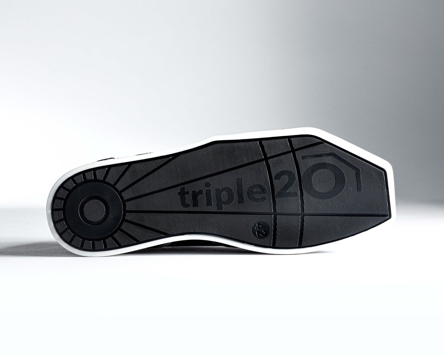 Detailaufnahme der Unterseite der Laufsohle eines triple20 Dartschuhs. Diese ist schwarz und präsentiert sich in einem vollendeten Design mit XXL Markenlogo, das sich über mehr als die Hälfte der Sohle erstreckt. Durch den weißen Sohlenrahmen wird die besondere Form der TPU-Sohle betont.