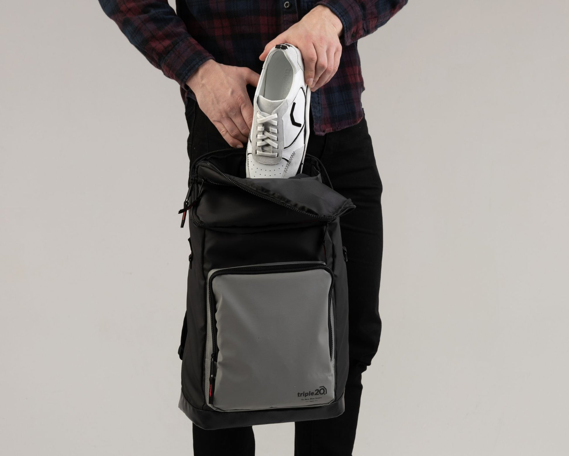 Produktfoto eines besonderen Schuhrucksacks für Dartschuhe. Auf dem Bild zeigt ein männliches Model, wie einfach sich genau ein Paar Dartschuhe im Rucksack durch die breite Öffnung verstauen lässt. Der Rucksack ist schwarz-grau mit feurig roten, sportiven Details.